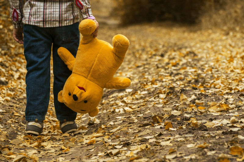 Ребенок идет по дороге и несет за ногу плюшевого медведя